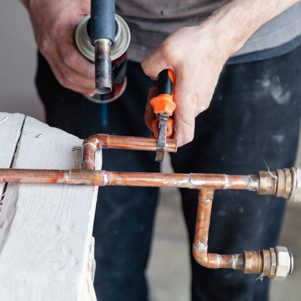 Closeup professional master plumber hands soldering copper pipes gas burner. Concept installation, plumbing replacement, solder flux paste, pipeline repair, professional plumber master, pipe leakage